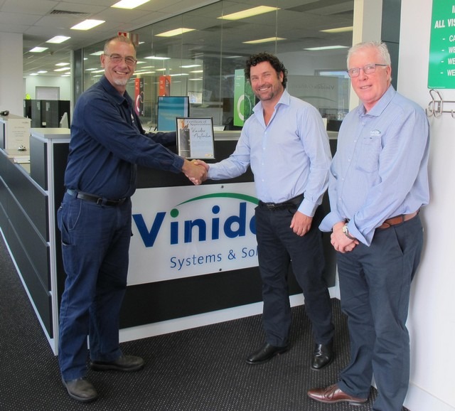 2 men shaking hands and one man watching