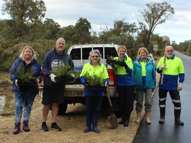 men and women standing infront of a ute holding seedlings