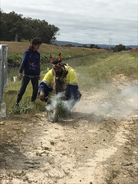 Aboriginal man performing smoking ceremony at Harvey River with girl looking on