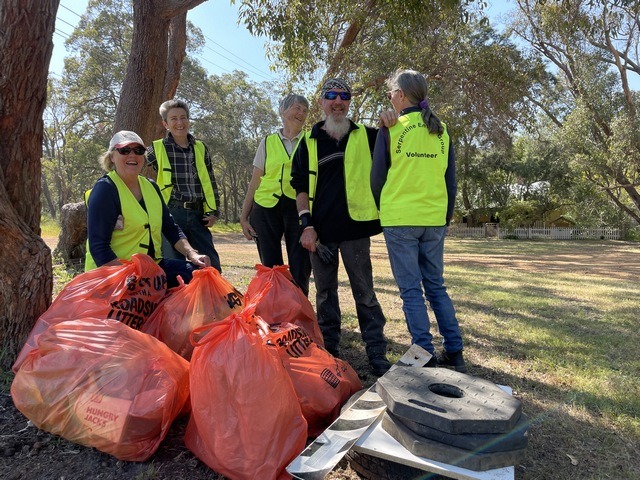 volunteers standing by bags of rubbish that they have collected in bushland